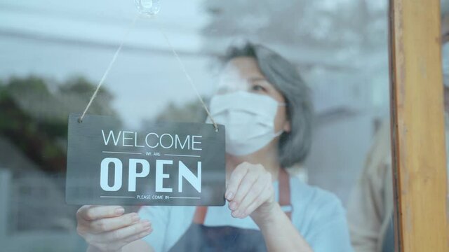 Asian Senior Couple wear mask turn Welcome sign to open restaurant. 