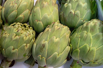 Obraz premium Flower buds of artichoke for sale at the Farmer's Market, edible part of the plant used in Mediterranean cuisine as a tasty vegetarian side dish, either steamed, marinated in olive oil or deep fried