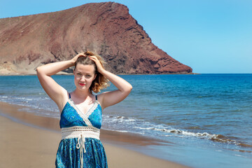 Beautiful Caucasian millennial woman at Playa La Tejita in a sunny summer day with miles of clean golden sand behind and the volcanic Montana Roja in the background in Tenerife, Canary Islands, Spain