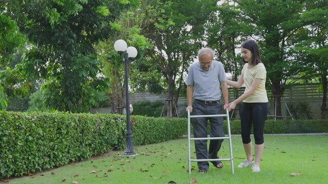 Asian girl help elderly handicaps man father walk with walker in park.
