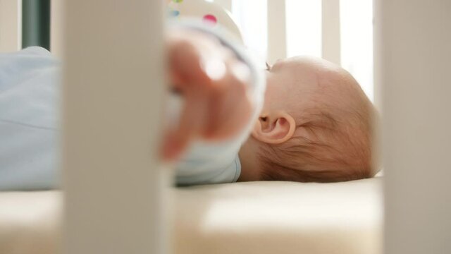 Baby lying in crib and holding wooden banister with hand. Baby in cot at nursery