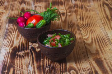 Salad of fresh spring vegetables in a clay bowl. Salad ingredients radish, tomato, cucumber, onion, parsley, dill on a brown wooden table