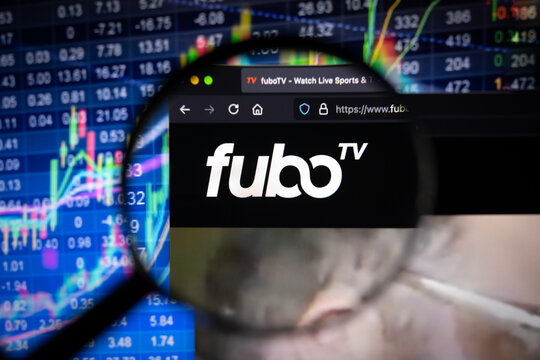 Fubo TV company logo on a website with blurry stock market developments in the background, seen on a computer screen through a magnifying glass