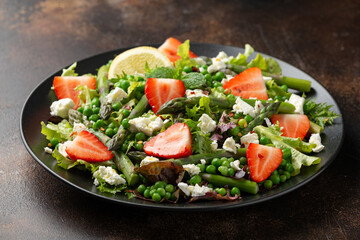 Asparagus and Strawberry Salad with vegetables, green peas and feta cheese in black plate. healthy food.