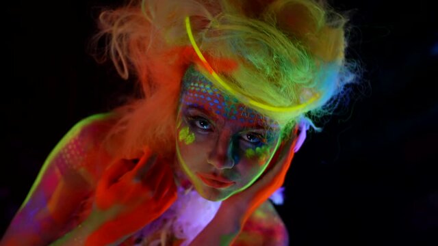 young woman with glowing makeup in ultraviolet light, fluorescent paints on face and body