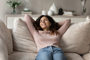 Smiling millennial Hispanic woman lying relaxing on couch at home sleep or take nap daydream. Happy...