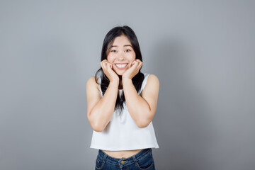 Portrait of Asian woman pillowing face on her hands wear white casual tank top isolated on gray background, feels cheerful to win prize, good news