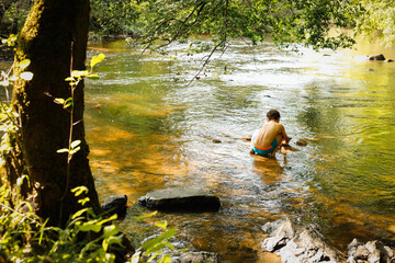 Young boy sitting and playing in the river back view