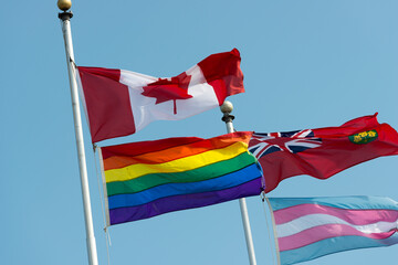 flags of Canada and Ontario flying above a red, orange, yellow, green, blue, and purple flag and a...