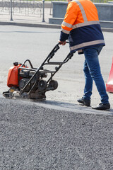 Fototapeta premium A road worker compacts fresh asphalt with petrol vibratory plate on a sunny day.