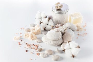 body and soul care, round stones, sea salt, salt soap, body peeling cream, cotton flowers on a white background