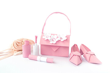 Origami paper background with shoes, bag, lipstick, nail polish and flowers. Handmade pink high heels isolated on white background. Origami composition. Paper craft. 