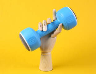 Wooden hand holding dumbbell on yellow background. Fitness concept