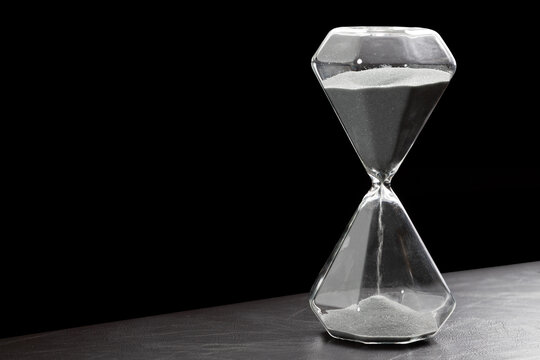 Sand running through the bulbs of an hourglass. grey sand are moving in hourglass.