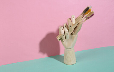 Wooden hand holding eco bamboo toothbrushes on blue pink pastel background. Trendy shadow. Concept art. Minimalism. Creative layout