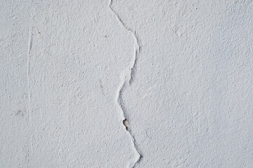 Cracked white paint texture. Crack in the middle of a white rough wall background.