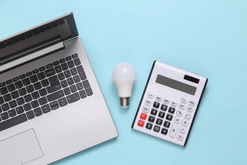 Laptop, Calculator and led light bulb on blue background. Top view. Flat lay.