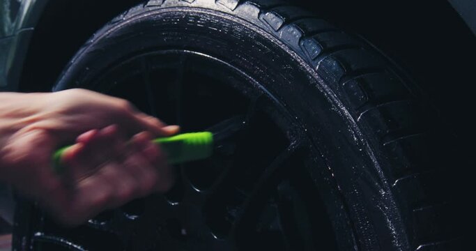 Worker using brush for cleaning surface of wheel at car wash. Close up of wheels cleansing. Detailing concept