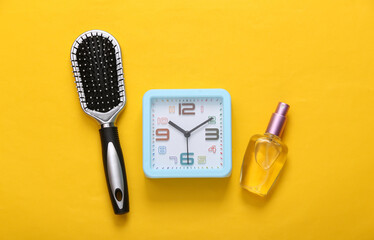 Alarm clock, comb and perfume bottle on yellow background