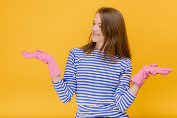 Attractive housewife woman wear rubber cleaning gloves and casual blue striped sweater hold hand offer object on open arms , body language home cleaning concept standing against a yellow background