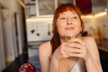 Woman sitting at the kitchen and holding glass of the orange juice