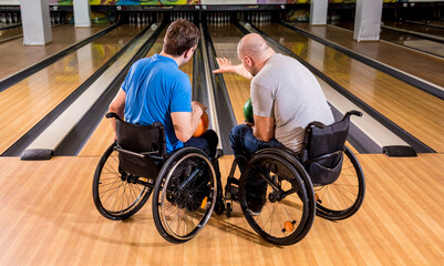 Two young disabled men in wheelchairs playing bowling in the club