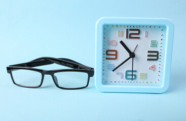 Alarm clock with glasses on blue background