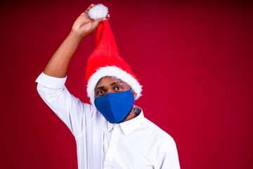 Fototapeta na wymiar african american man in santas hat wearing mask in red studio background