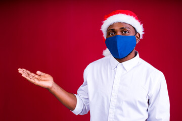 african american man in santas hat wearing mask in red studio background