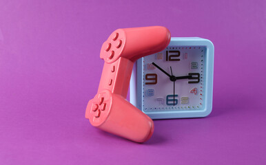 Alarm clock and joystick on purple background. Time to play video games