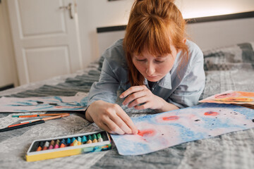 Happy woman looking at her painting while laying at the bed