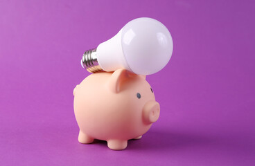 Light bulb and piggy bank on purplr background close up. Save money