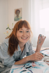 Beautiful red haired woman painting in her cozy bedroom