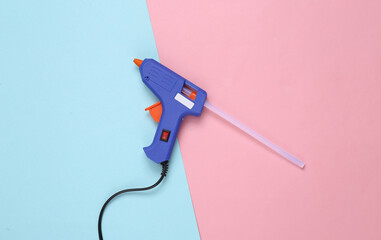 Glue gun with glue stick on a pink blue background. - obrazy, fototapety, plakaty