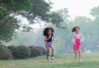 Adorable Afro girl and Asian girl running competition with fun in green park on holiday, group of primary school friendship laughing play in garden, kids exercise spent time with nature play together
