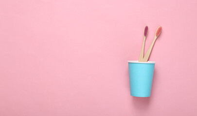 Two eco bamboo toothbrushes in cardboard cup on pink background