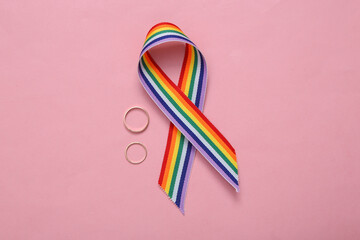 LGBT rainbow ribbon pride tape symbol with golden wedding rings on pink background.