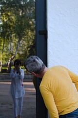 Man in yellow t-shirt looks on reflection in window at photographer standing behind