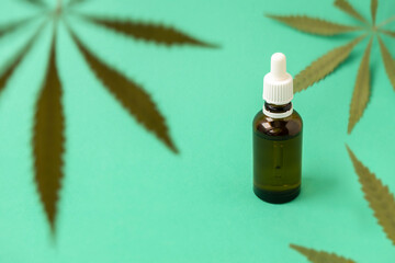 Green marijuana leaves on green background with cannabis oil in a glass bottle, selective focus. Cannabis for medicinal purposes concept