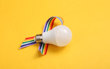 Light bulb with LGBT rainbow ribbon pride tape symbol on yellow background.