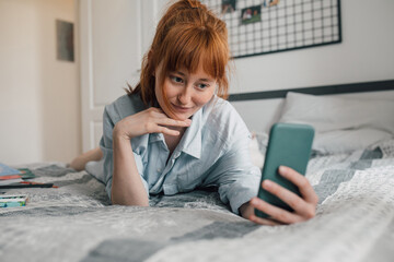 Ginger girl relaxing at home, holding cell phone and taking selfie