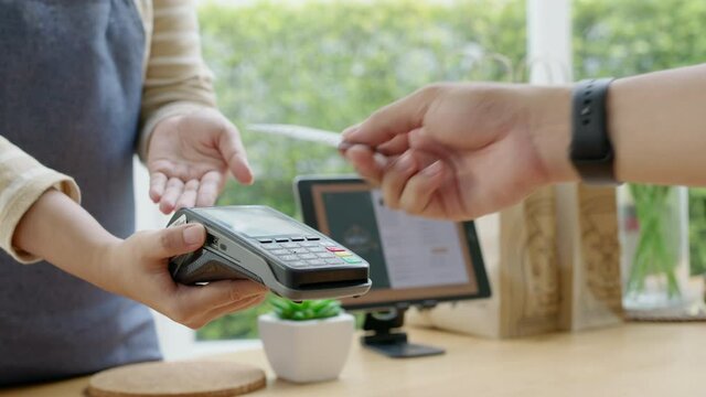 Close-up hand asia woman people work in small sme coffee cafe shop store owner use cashless wifi paywave nfc scan app smart pos reader sale in take out food drink order in urban city life contactless.