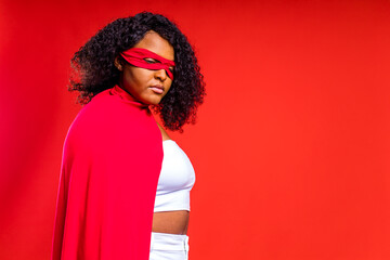 spanish woman in eye mask and superhero cloak in red studio background