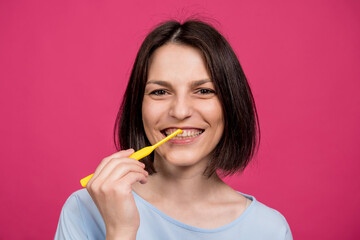 Beautiful happy young woman with single tufted toothbrush on blank pink background
