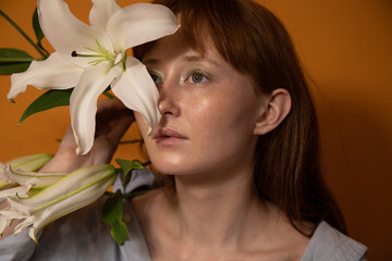 Ginger woman hiding her face behind the flowers while posing at the studio