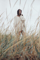 Beautiful stylish woman with windy hair in knitted sweater posing among wild grass. Carefree...
