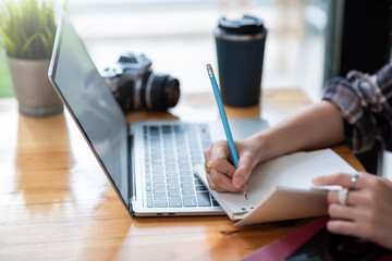 Close-up of a businesswoman hand holding a pencil taking notes using a laptop placed on the office desk.