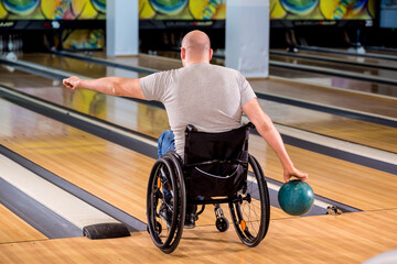 Young disabled man in wheelchair playing bowling in the club