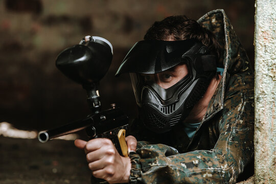 Young man in a paintball action with professional equipment, mask, gun and protective helmet, simulate military combat using air guns to shoot capsules of paint at each other