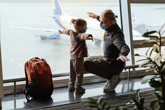 Man With Girl Ready To Fly By Airplane And The Airport. Father And Child Looking Though The Lounge Window On Plane With Backpack. Copy Space, Safe Family Travel In Face Mask During Covid-19 Quarantine